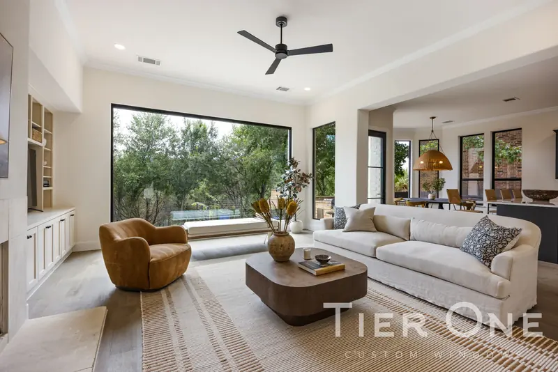 Full-width black-framed picture window in a living room looking onto oak trees